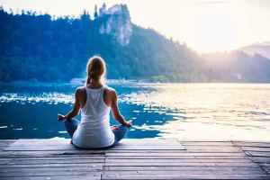 Frau sitzt auf einem Steg am See und meditiert